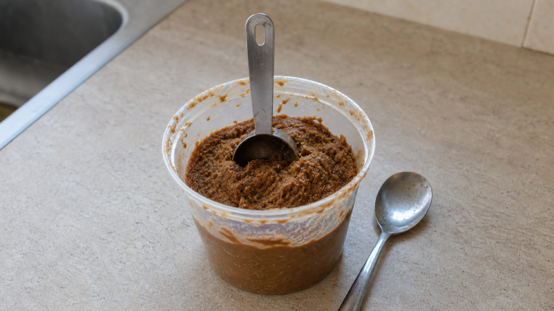 A measuring spoon stuck upright in a tub of miso paste (illustration)